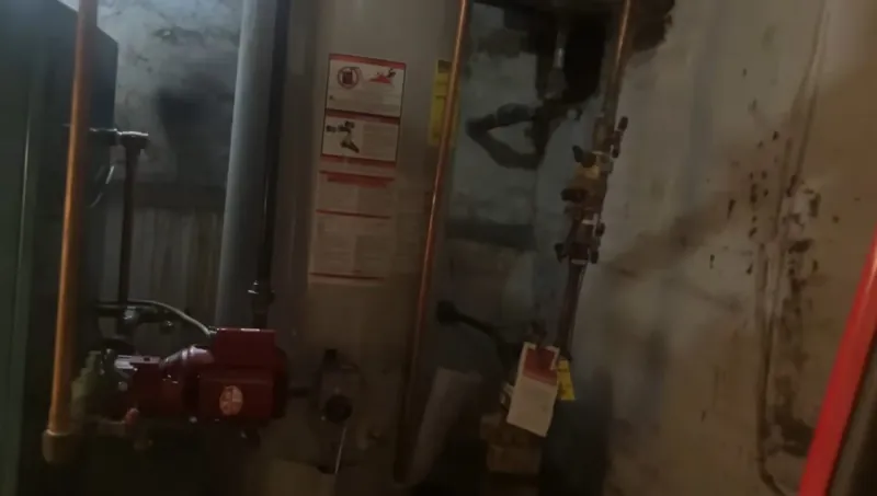 Basement mechanical room with a red circulator pump, copper piping and tags on the wall