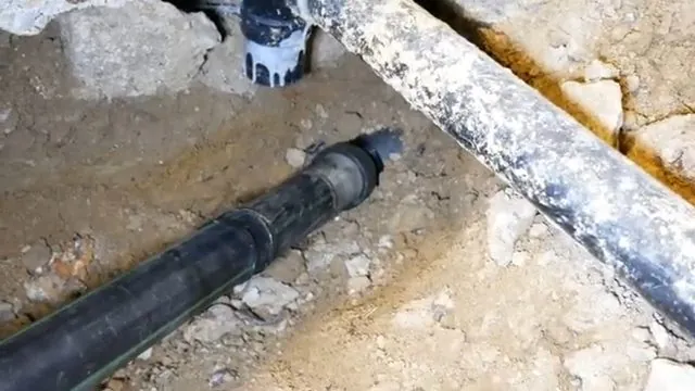 Black pipe liner section exposed in a trench alongside a length of white pipe
