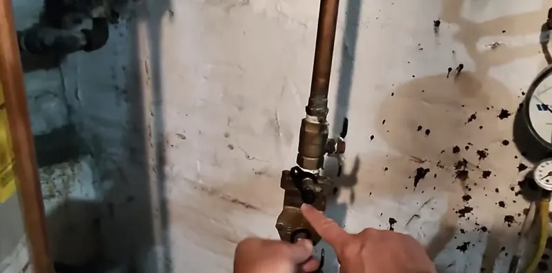 Brass valve and copper pipe on a white wall splattered with dark sediment next to a pressure gauge