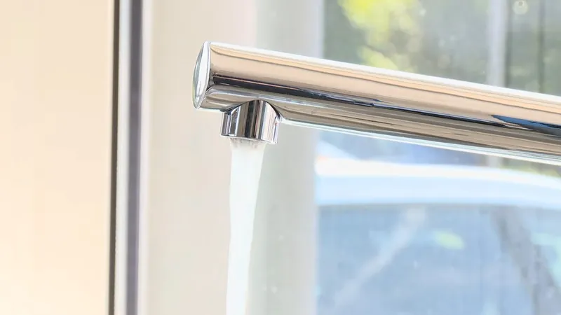 Chrome kitchen faucet running a stream of water beside a sunlit window