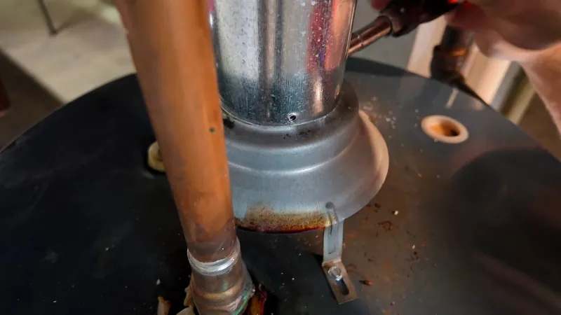 Copper supply pipe and a silver flue collar on top of a black water heater with a rust stain