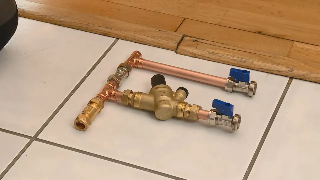 Copper tee fitted with two blue-handled ball valves and a brass regulator laid on a tile floor