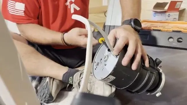 Hands holding a garbage disposal sideways with a drain hose and electrical cord at the side