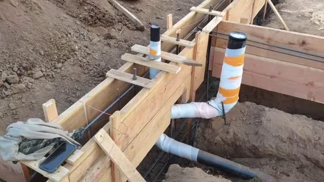 Wooden foundation forms with white PVC stub-outs wrapped in orange tape rising out of the dirt