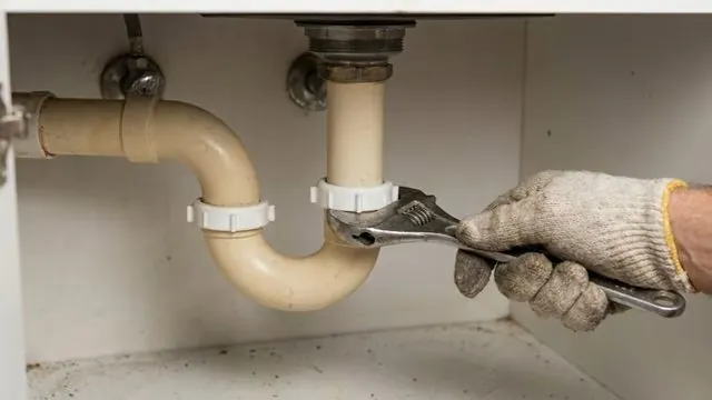 Gloved hand turning a wrench on a slip nut of a beige P-trap under a sink