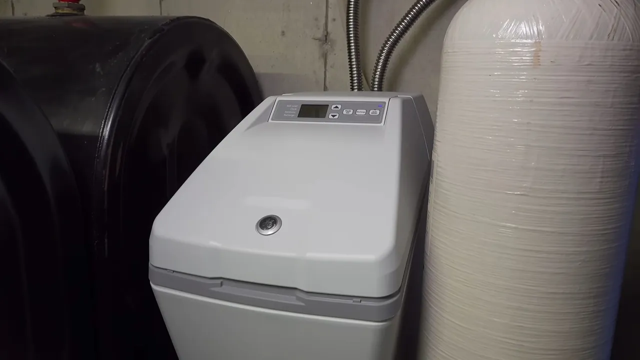 Gray residential water softener cabinet beside a black brine tank and a white resin tank against a garage wall