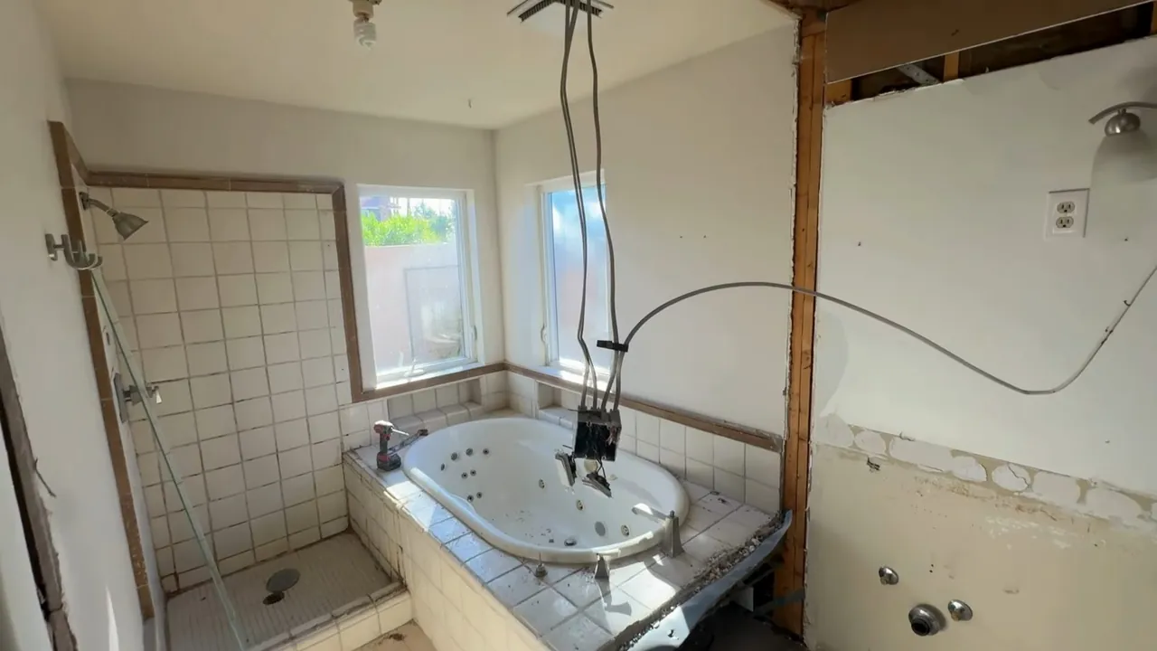 Gutted bathroom with tile walls, a corner tub and cables hanging from an opened ceiling