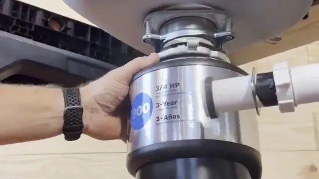Hand holding a three-quarter horsepower garbage disposal installed under a sink with a white drain pipe