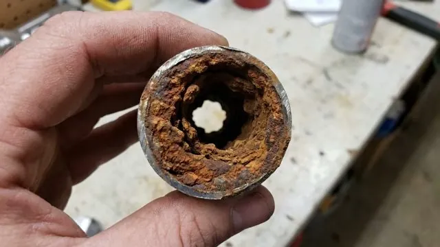 Hand holding a short pipe section with a narrow rust-lined bore packed with scale