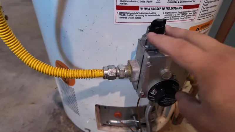 Hand reaching to a water heater gas valve with a yellow flexible gas connector attached