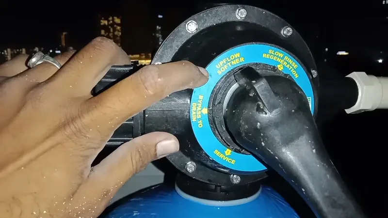 Hand turning the blue-ringed control valve head on top of a blue softener tank at night