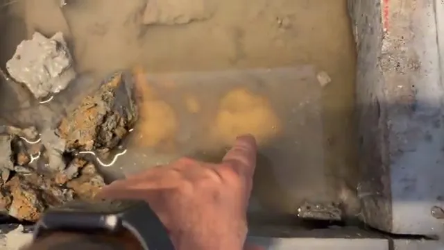 Hand pointing at a hole in a concrete slab where water sits at the bottom among broken pieces