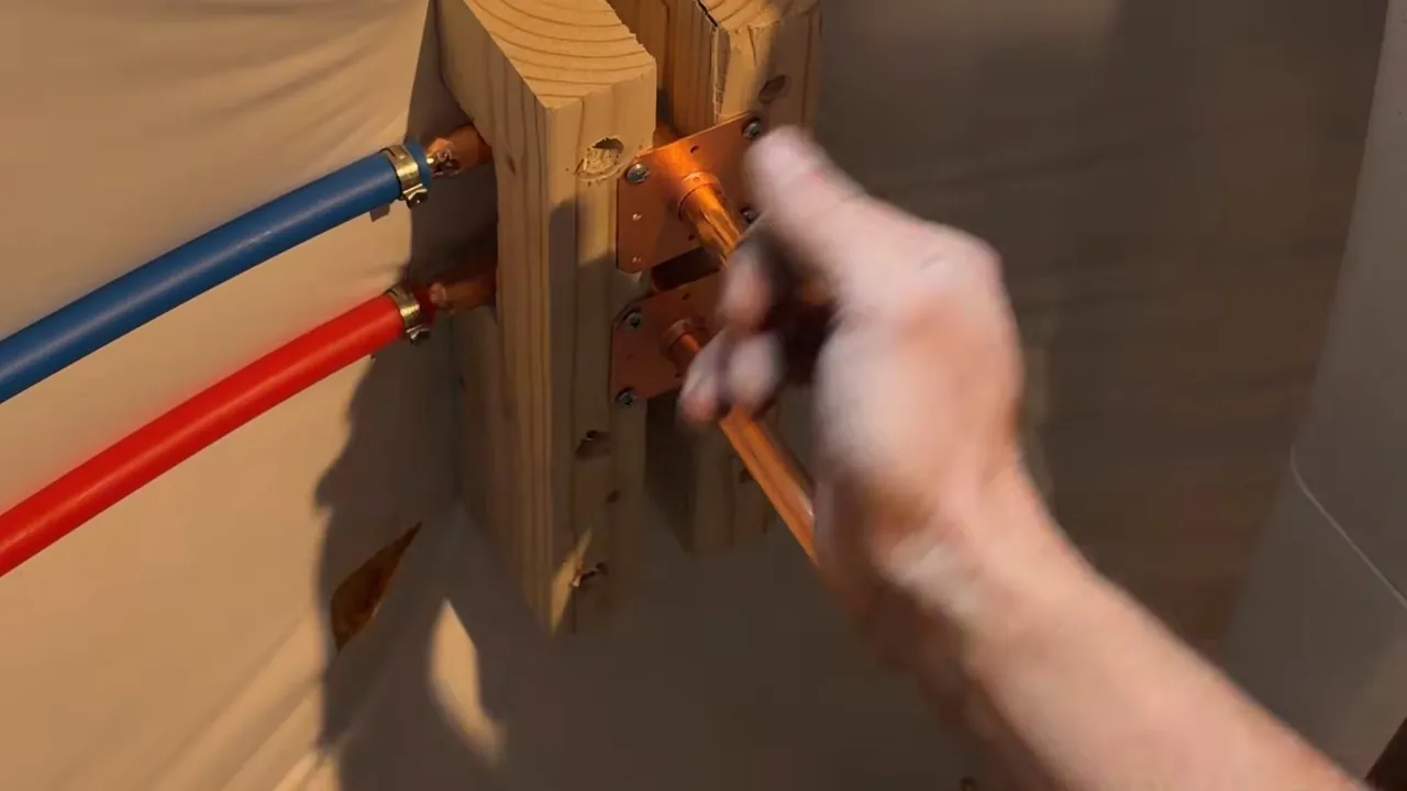 Hand working a copper fitting on red and blue PEX lines mounted to a wood block