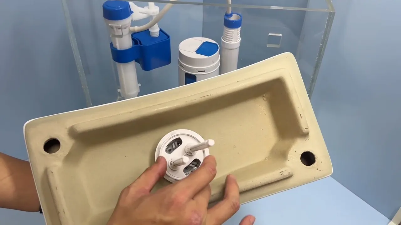 Hands holding a toilet tank lid upside down while fitting a white flush valve piece through it