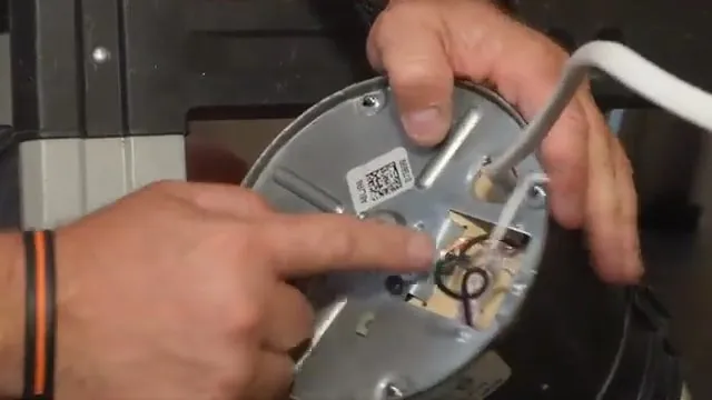 Hands pointing at the wiring and element plate of an electric water heater with the cover off