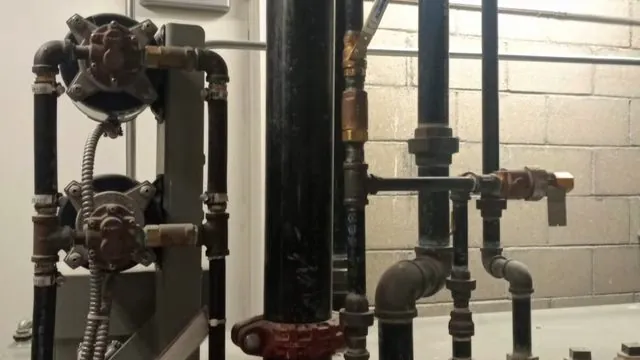 Old black iron pipes with round-handled valves mounted on a cinder block wall in a basement
