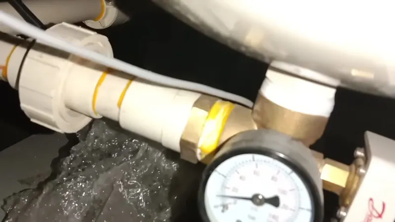 Pressure gauge screwed into a brass regulator fitting with PVC pipe and splashing water behind it