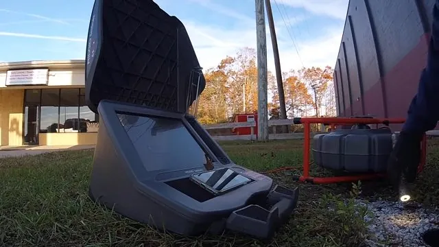 Open sewer inspection camera reel case sitting on grass beside a parking lot