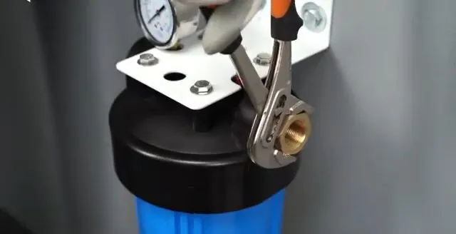 Wrench on the bolts of a whole-house blue filter housing with a pressure gauge on top